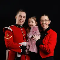 A man in a red military uniform holding a young girl in a pink dress, standing next to a woman wearing the same attire.