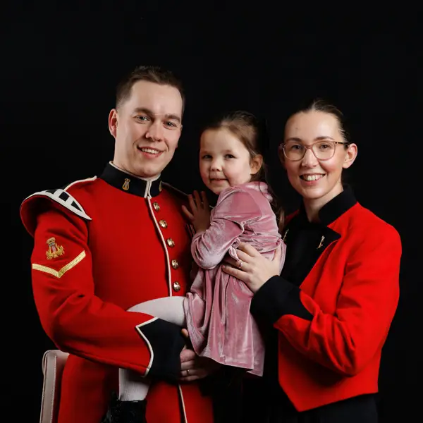 A man in a red military uniform holding a young girl in a pink dress, standing next to a woman wearing the same attire.
