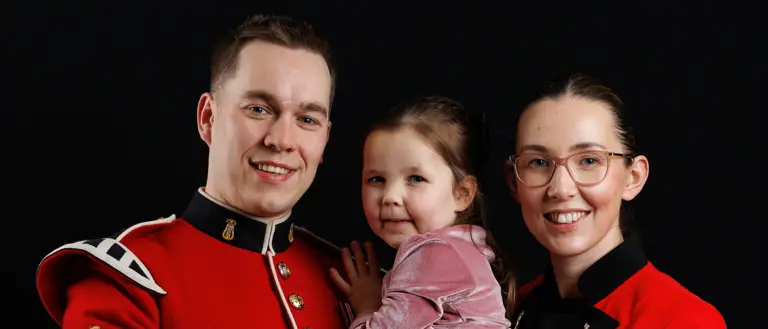 A man in a red military uniform holding a young girl in a pink dress, standing next to a woman wearing the same attire.