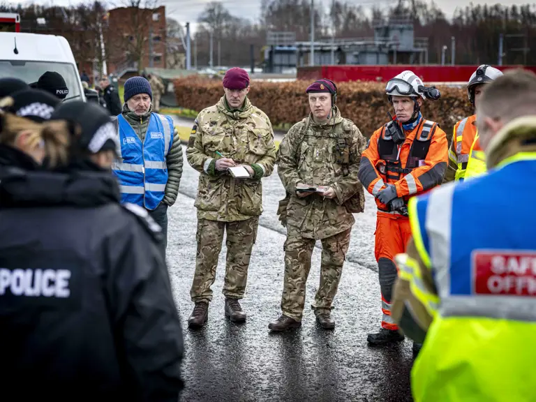 Group of uniformed personnel including police, military, and safety officers gathered outdoors for a briefing.