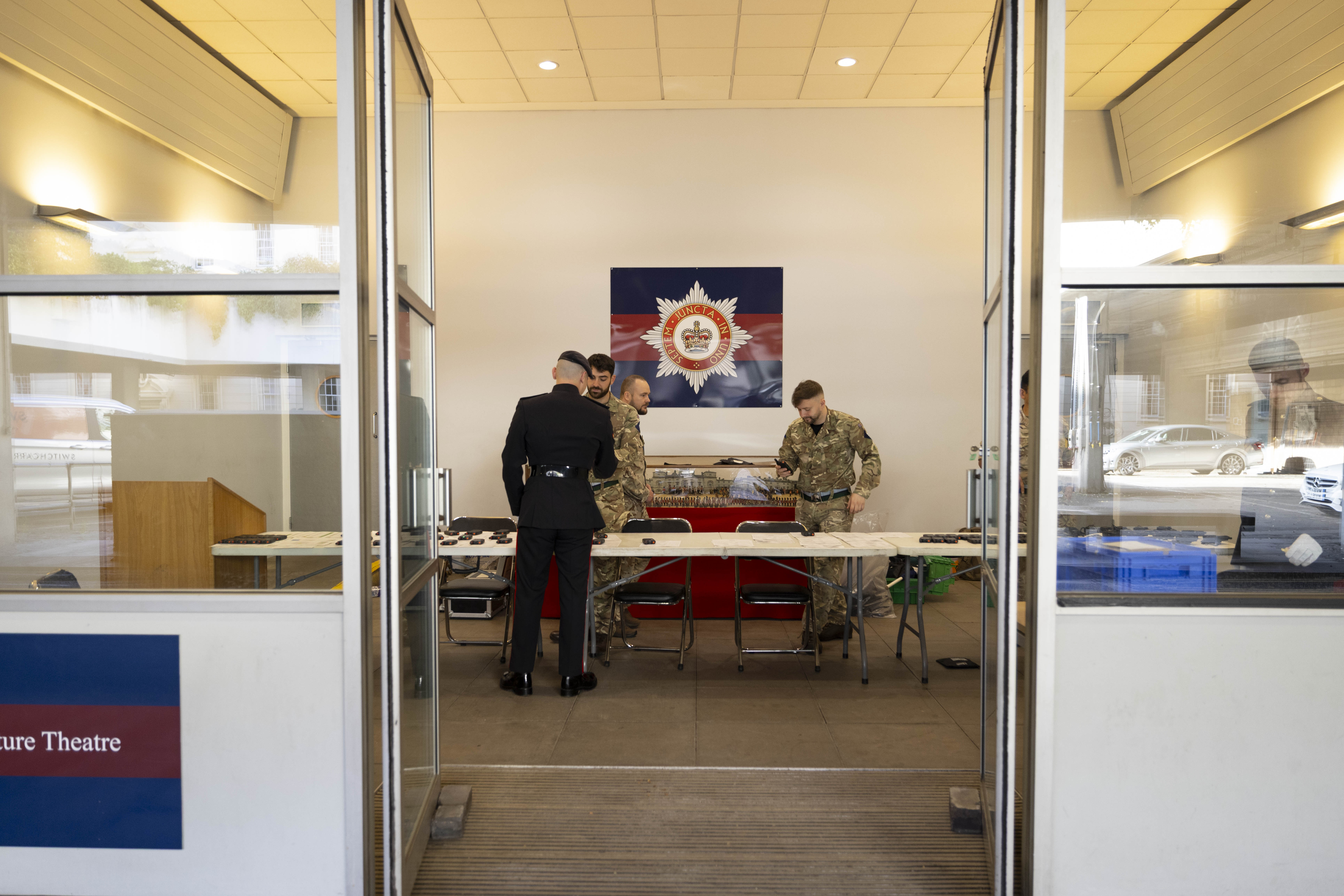 Four people in military uniforms stand around a table inside a room with a police emblem on the wall. The mood is focused and professional.