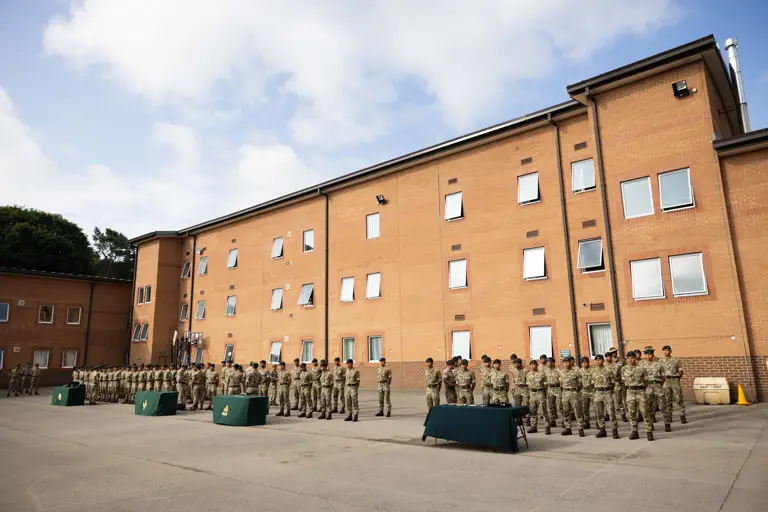 Rows of soldiers in camouflage uniform stand in rows in front of a brick building 