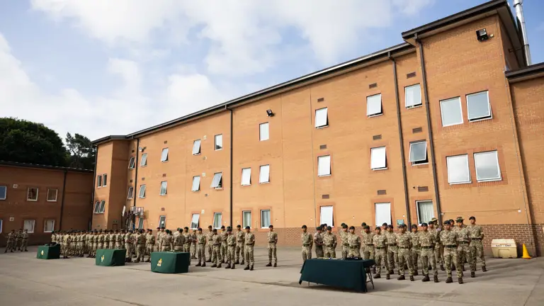 Rows of soldiers in camouflage uniform stand in rows in front of a brick building