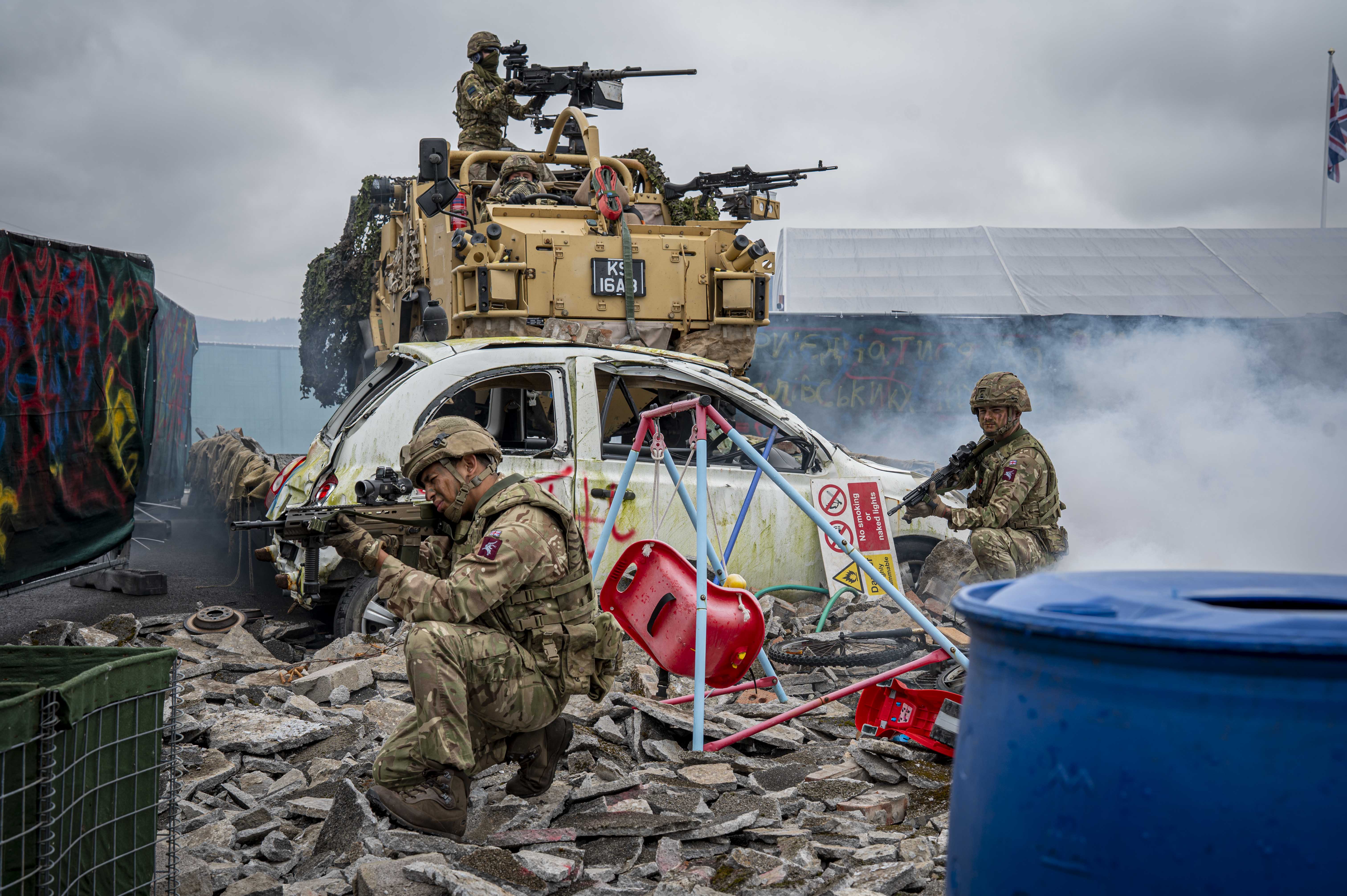 Soldiers shown demonstrate an attack scenario outside with debris including a child's swing, a car and white goods and a jackal with Soldiers in coming through the back.