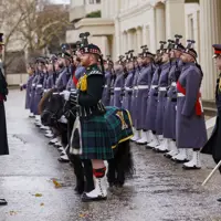 A line of uniformed guards standing at attention outside of a historic building.