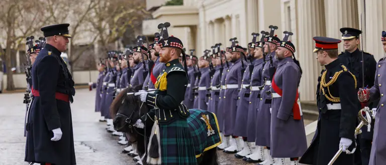 A line of uniformed guards standing at attention outside of a historic building.