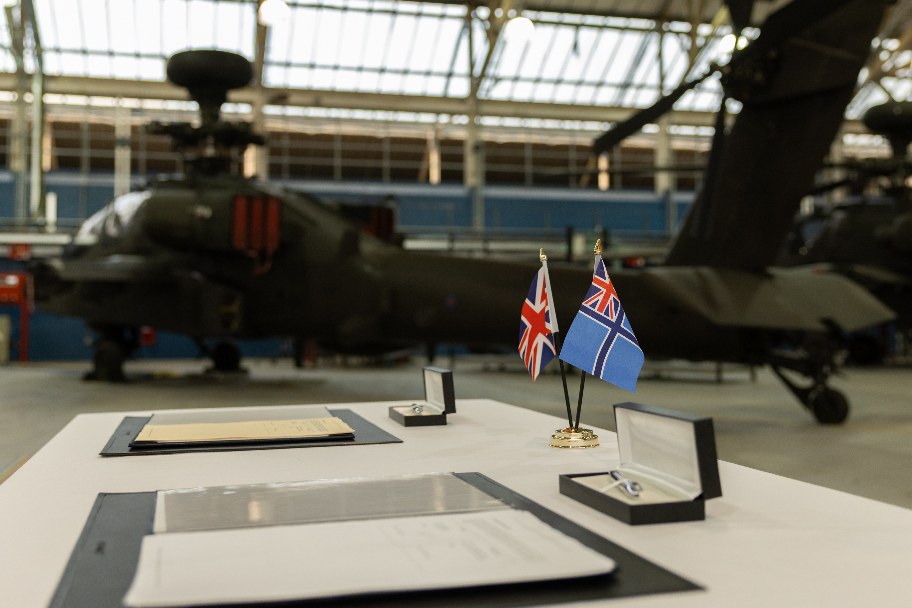 Some documents and flags sit on a table in front of a green military helicopter.