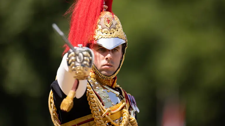 A soldier in black ceremonial attire points his swords towards the camera.