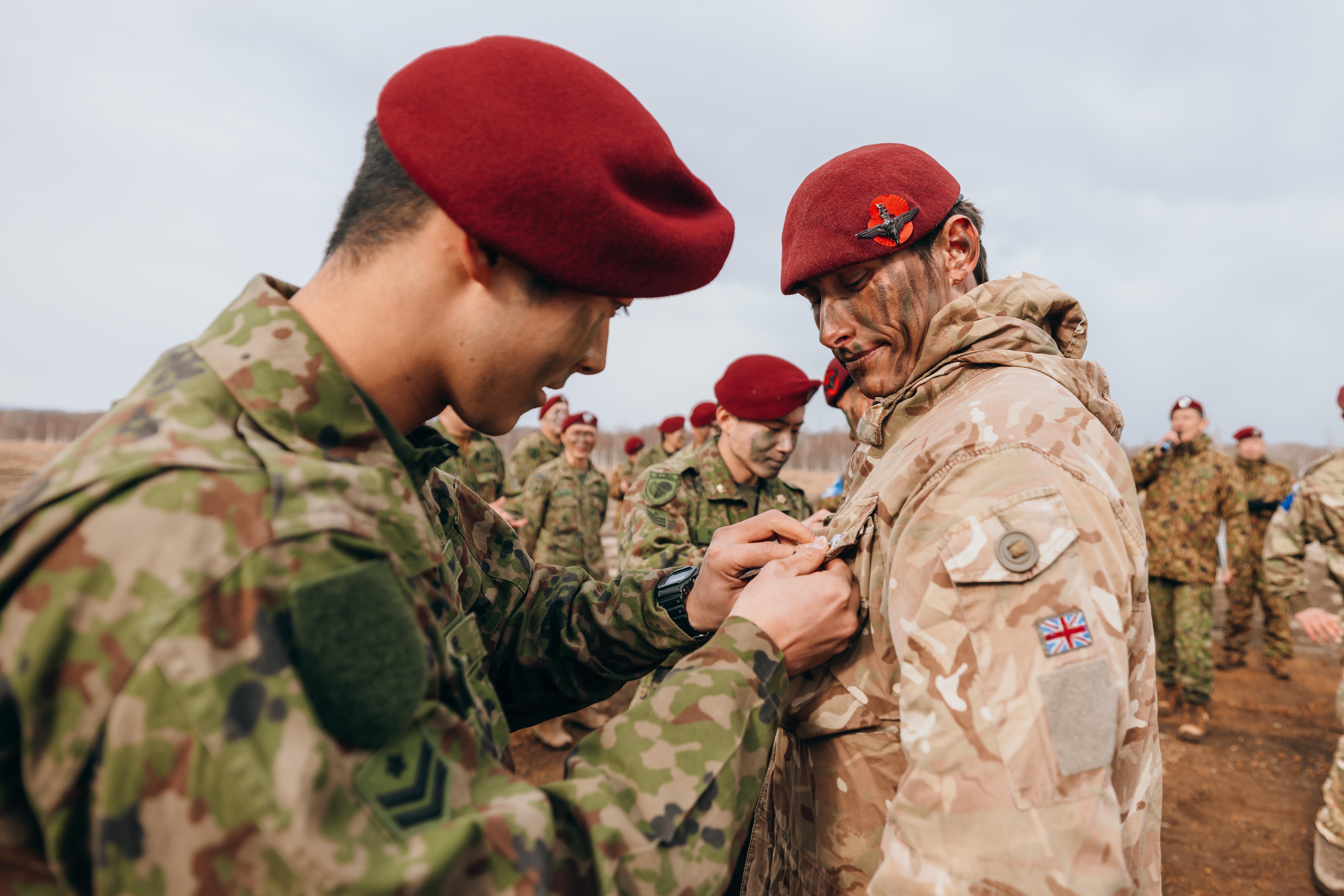 Soldiers in camouflage uniforms and red berets participate in a pinning ceremony outdoors.