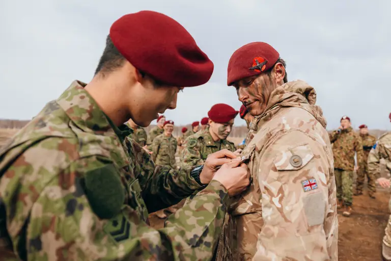 Soldiers in camouflage uniforms and red berets participate in a pinning ceremony outdoors.