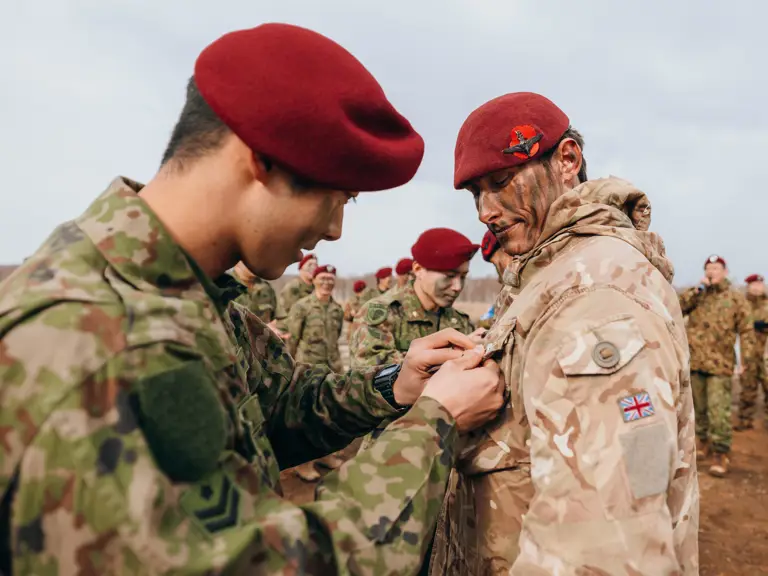Soldiers in camouflage uniforms and red berets participate in a pinning ceremony outdoors.