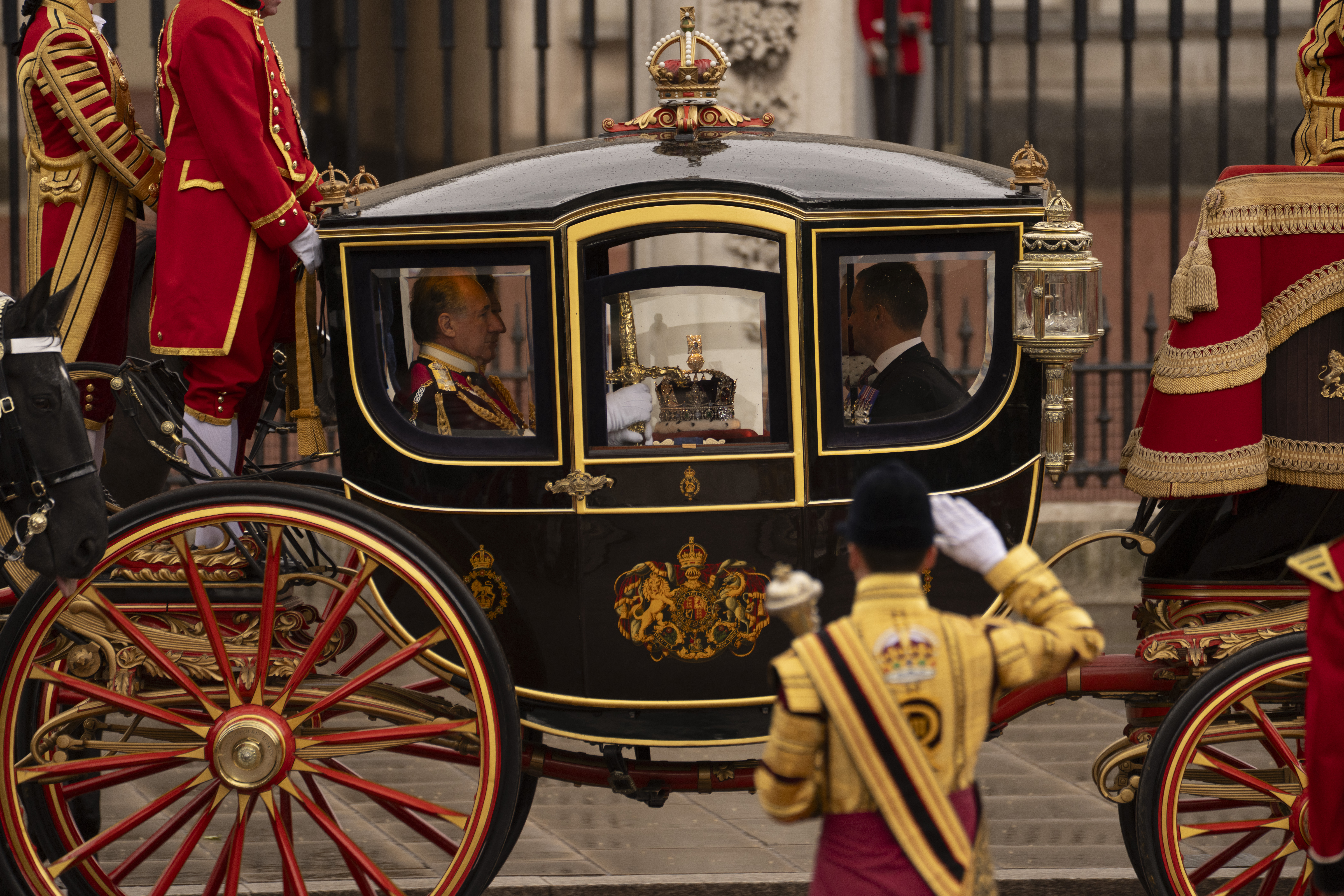 A regal horse-drawn carriage, intricately decorated in black and gold, is seen moving along a street. 