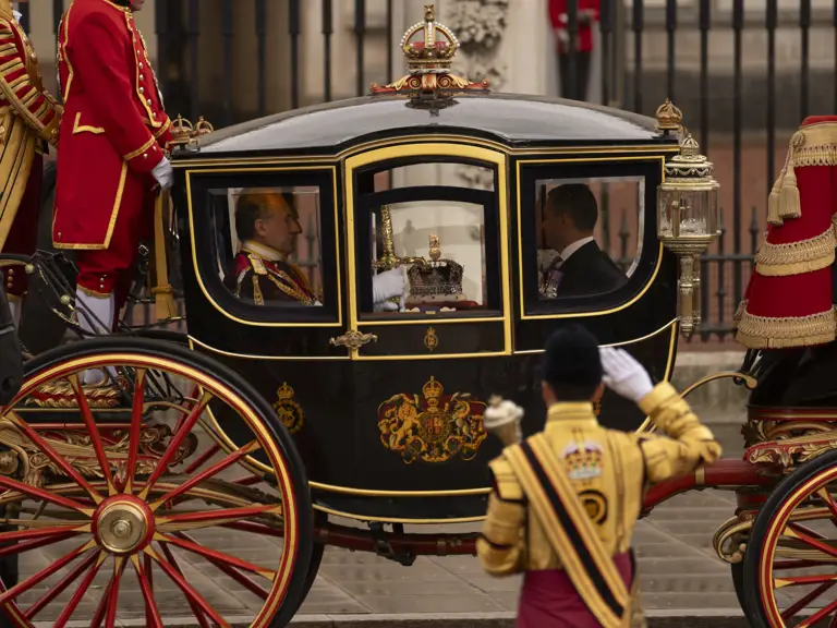 A regal horse-drawn carriage, intricately decorated in black and gold, is seen moving along a street.