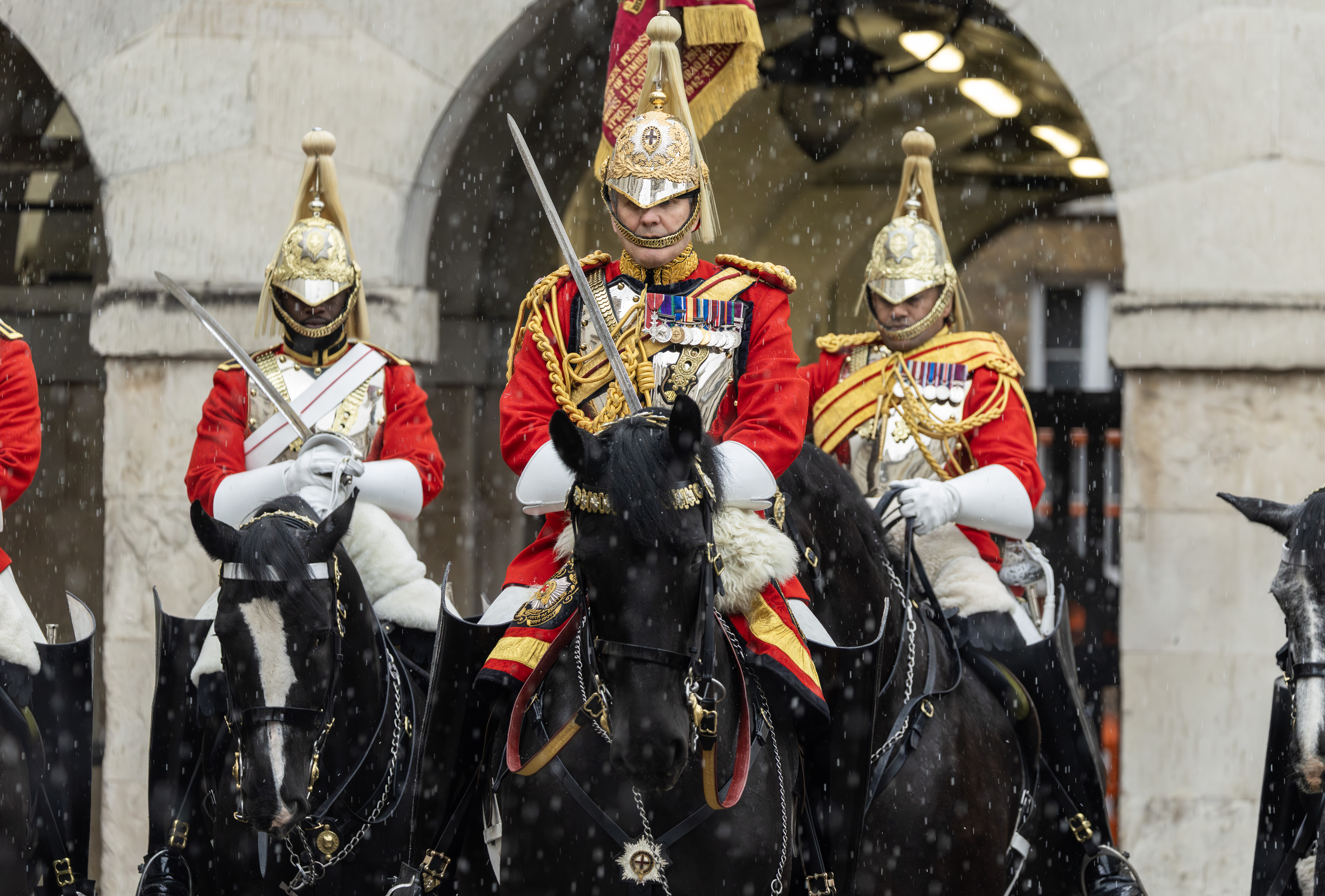 Members of the Household Cavalry in ceremonial uniform, including gold helmets and red tunics, riding black horses.