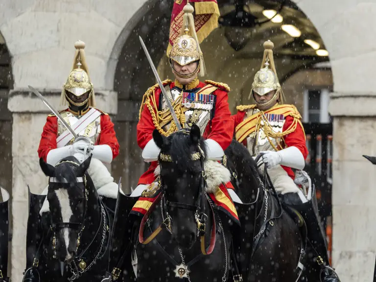 Members of the Household Cavalry in ceremonial uniform, including gold helmets and red tunics, riding black horses.
