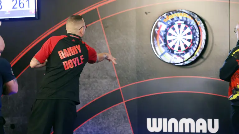 Dart player Danny Doyle aiming a dart at a dartboard during a match.
