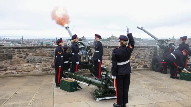 Several soldiers stand by as artillery is fired from a castle.