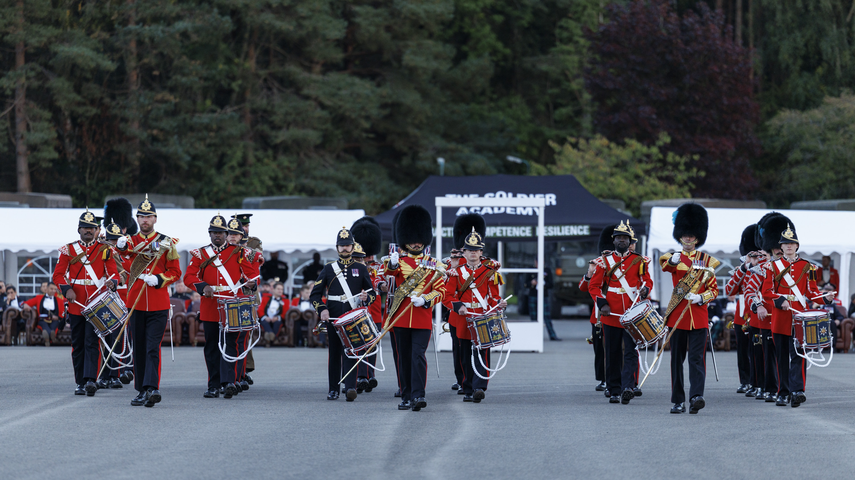 An Army band in red and black ceremonial uniform playing instruments. 