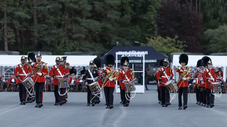 An Army band in red and black ceremonial uniform playing instruments.