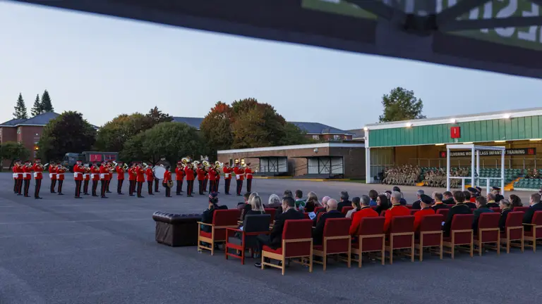An Army band in red and black ceremonial uniform playing instruments.