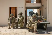 Two British soldiers and an Australian soldier kneel in front of a small green vehicle.