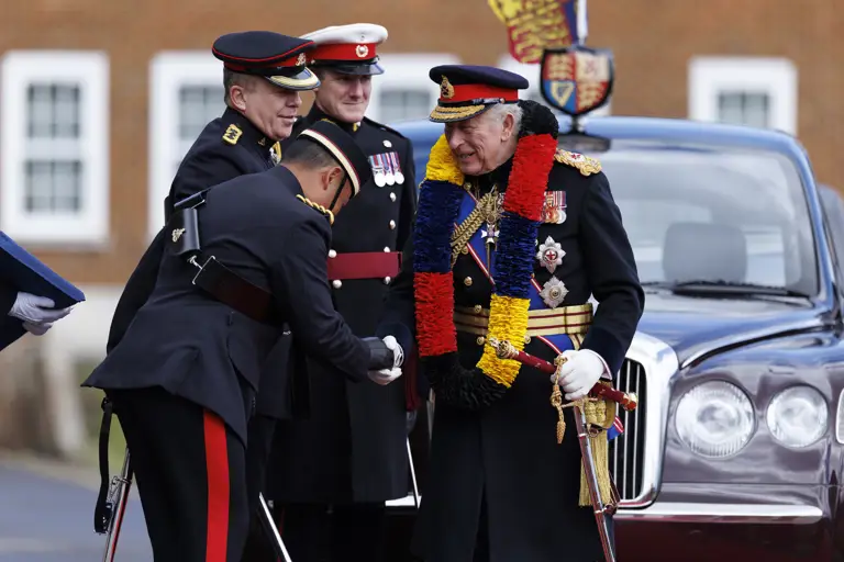 A group of uniformed individuals are standing in front of a parked car with a regal emblem.