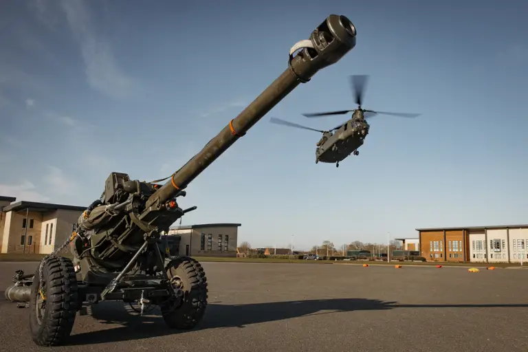 Artillery weapon is waiting to be attached the the underslung of a chinook flying into barracks for transport.