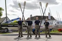 Four female soldiers in uniform from the waist down holding their rowing oars in the air.