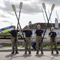 Four female soldiers in uniform from the waist down holding their rowing oars in the air.