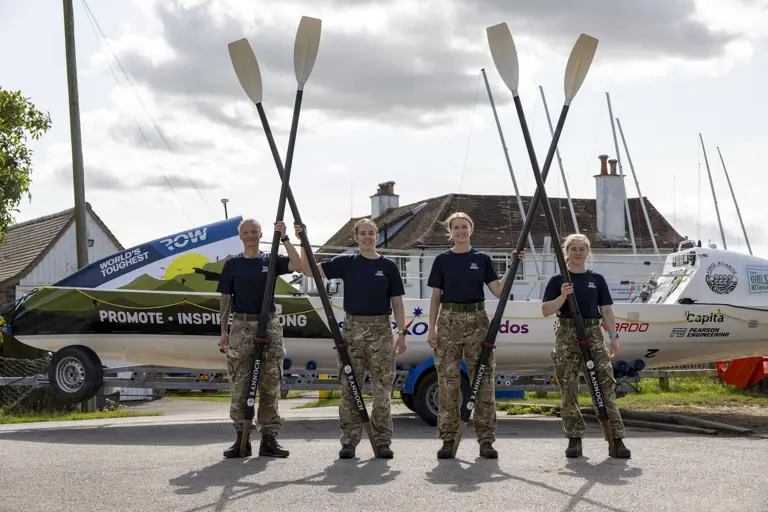 Four female soldiers in uniform from the waist down holding their rowing oars in the air.