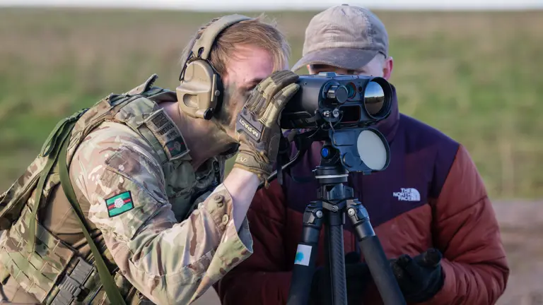 A soldier looks through some binoculars.