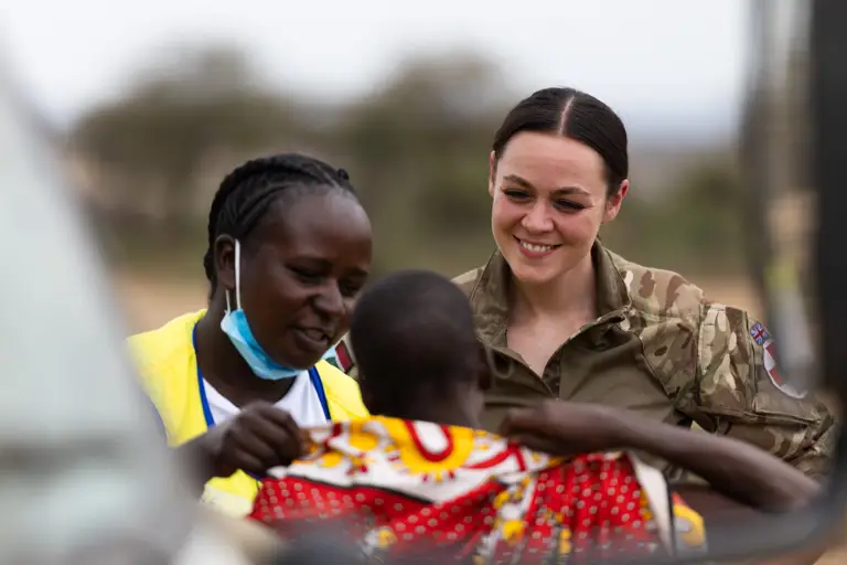 A British soldier in uniform smiles at a child.