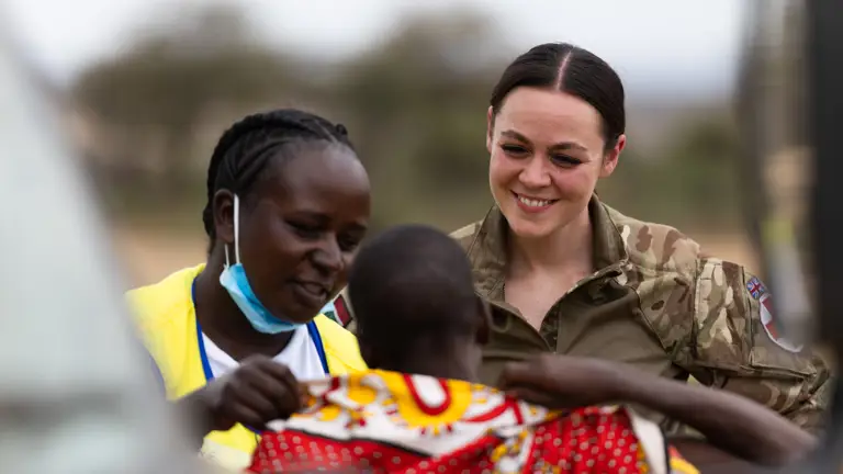 A British soldier in uniform smiles at a child.