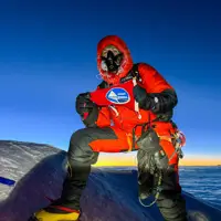 A man in red climbing gear and altitude mask is pictured on top of Mount Everest.