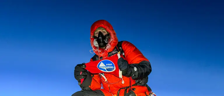A man in red climbing gear and altitude mask is pictured on top of Mount Everest.