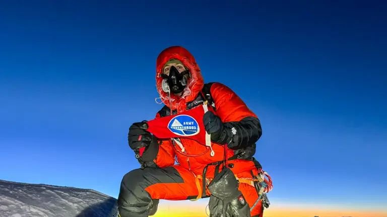 A man in red climbing gear and altitude mask is pictured on top of Mount Everest.