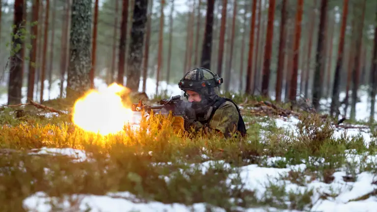 Soldier in camouflage and helmet fires a weapon in snowy forest, creating a bright muzzle flash. The scene conveys urgency and focus.