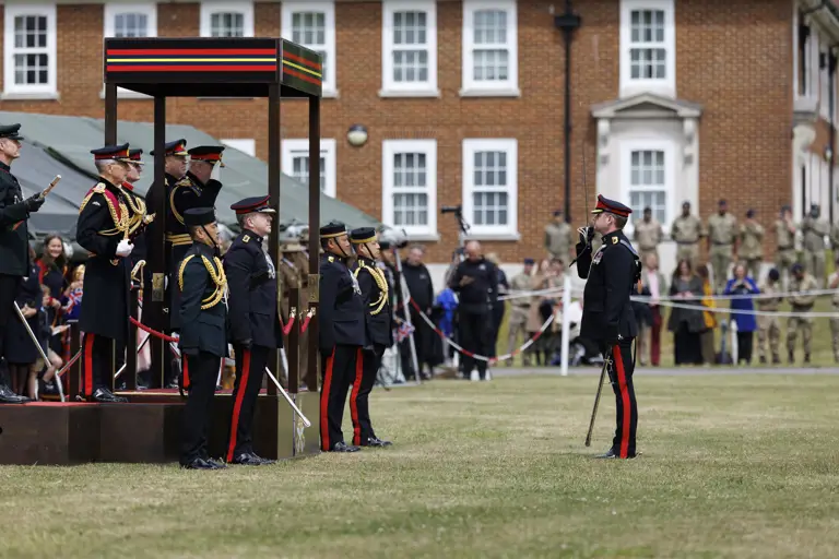 A ceremonial event with uniformed individuals standing in formation on a grassy field. A person salutes.