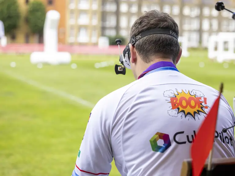 A man sits with his back to the camera whilst controlling a drone.