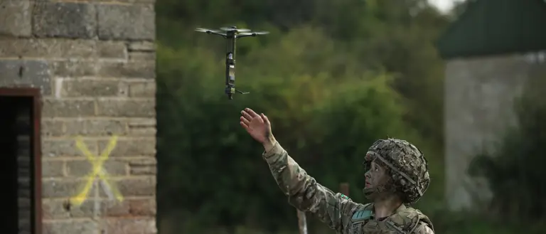 A man in uniform launches a drone into the sky.