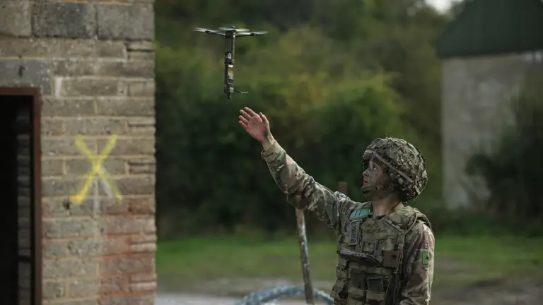 A man in uniform launches a drone into the sky.