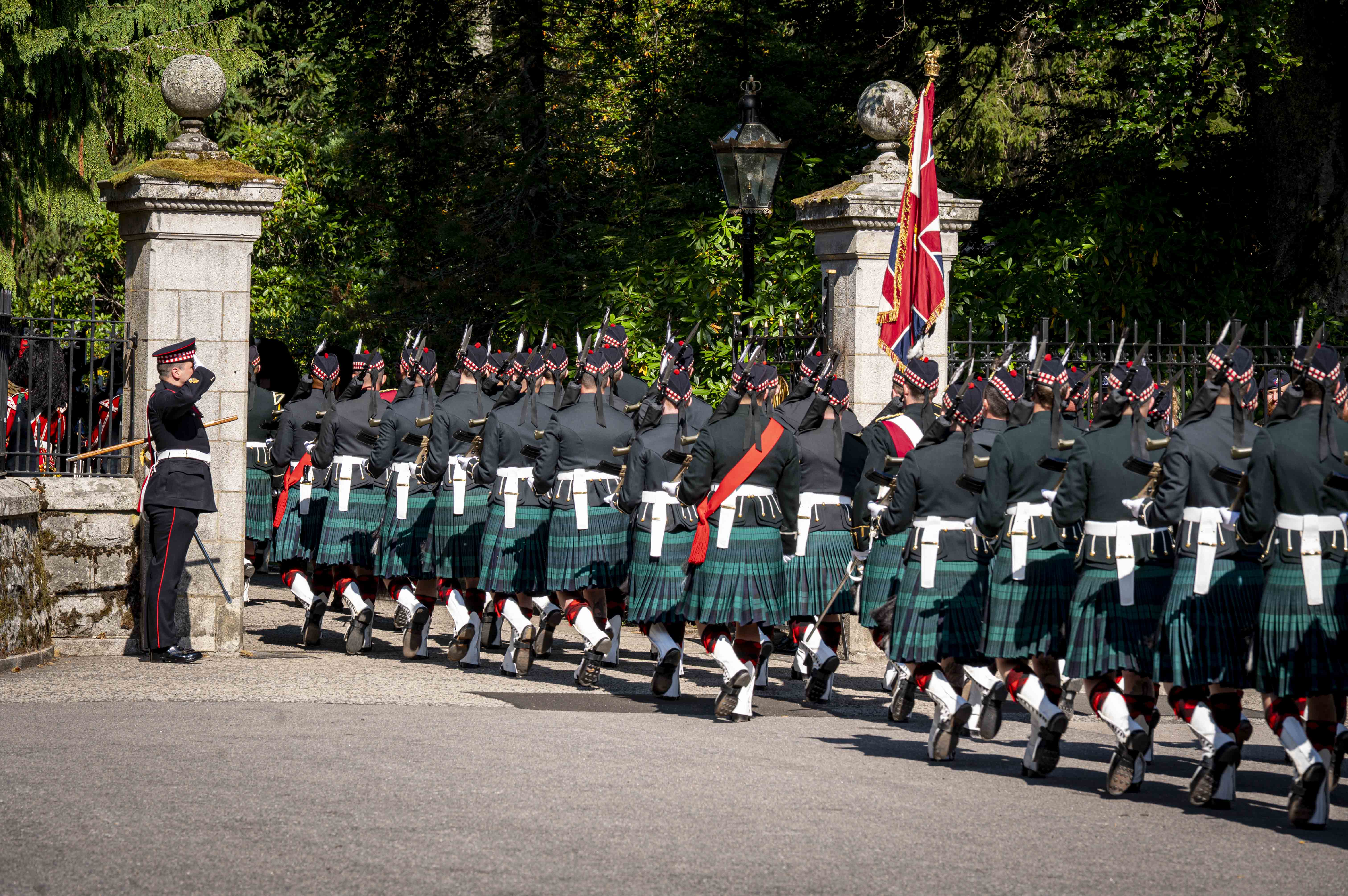 Soldiers in Tartan kilts march with their weapons raised. 