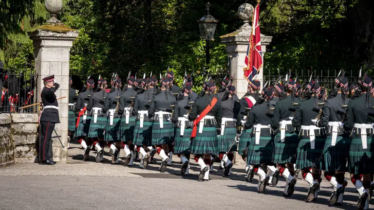 Soldiers in Tartan kilts march with their weapons raised.