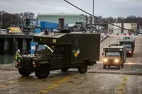 Green military vehicles are pictured driving through a port.