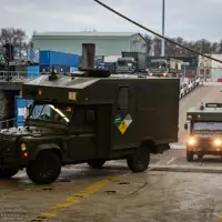 Green military vehicles are pictured driving through a port.