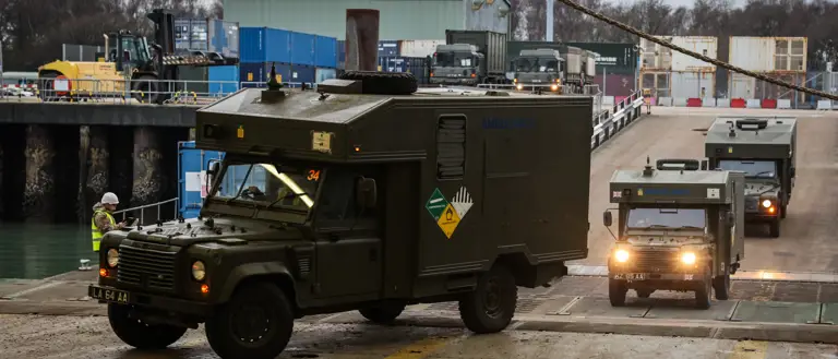 Green military vehicles are pictured driving through a port.