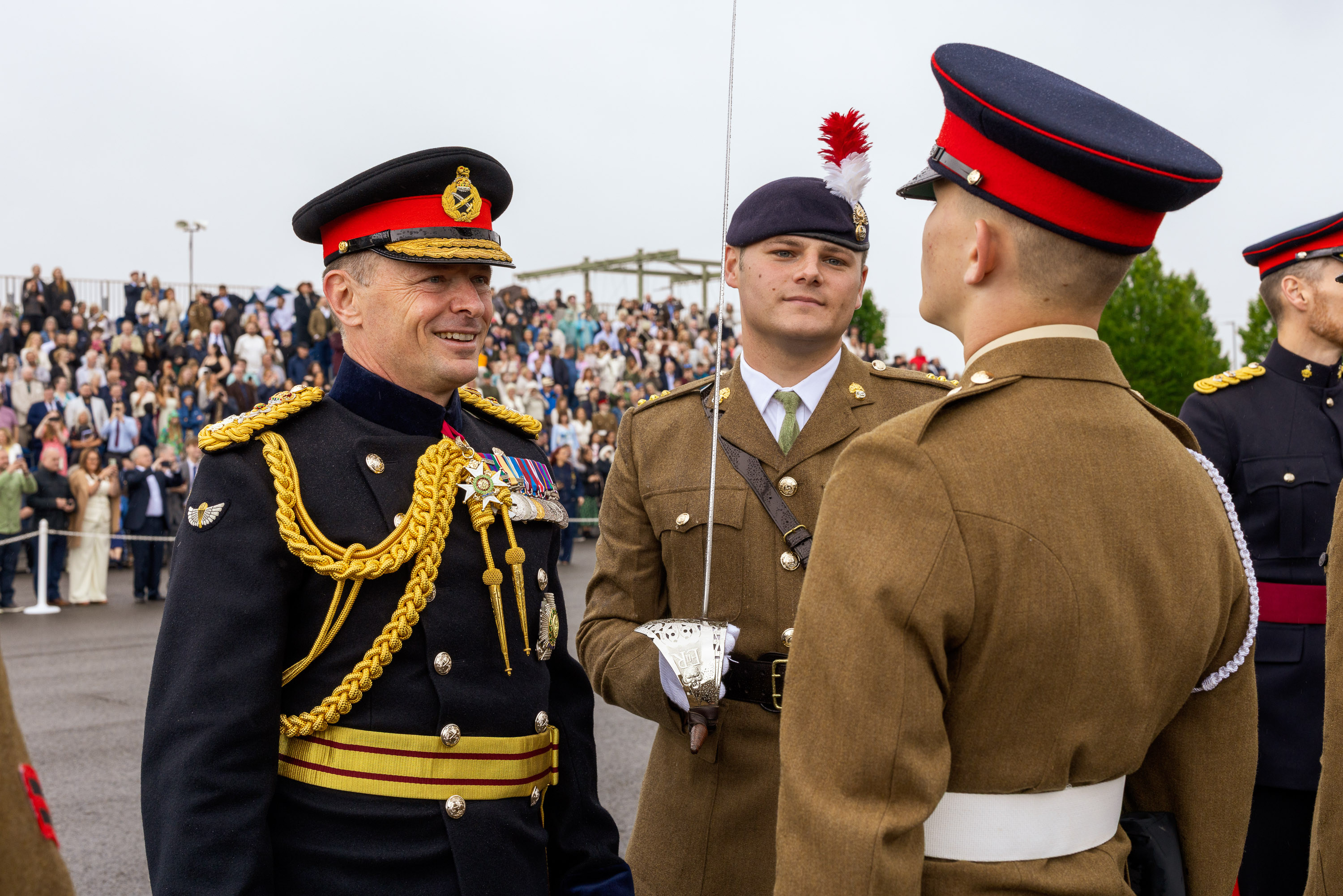 Chief of the General Staff in his blues uniform is photographed inspecting a soldier in their brown uniform while smiling. 