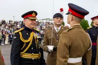 Chief of the General Staff in his blues uniform is photographed inspecting a soldier in their brown uniform while smiling.