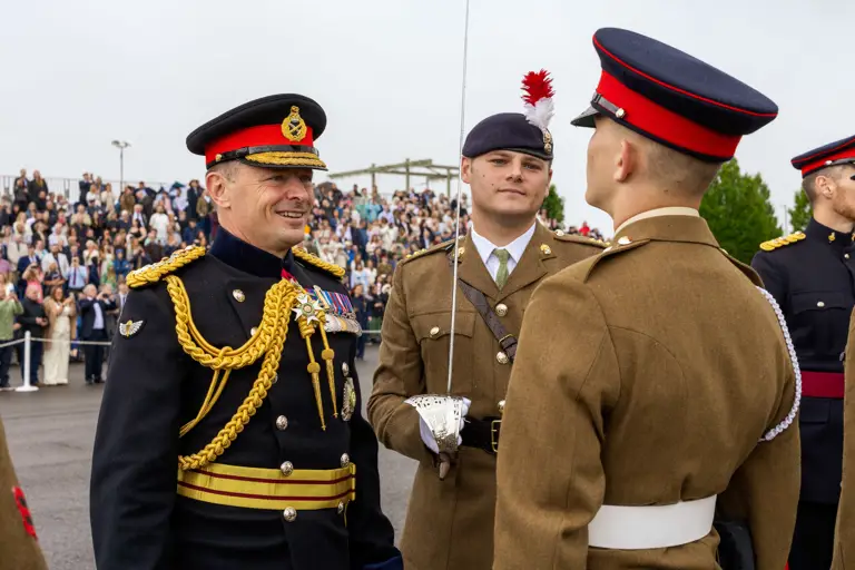 Chief of the General Staff in his blues uniform is photographed inspecting a soldier in their brown uniform while smiling.
