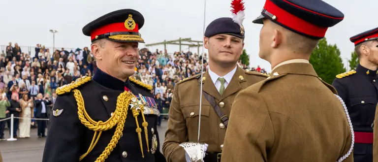 Chief of the General Staff in his blues uniform is photographed inspecting a soldier in their brown uniform while smiling.